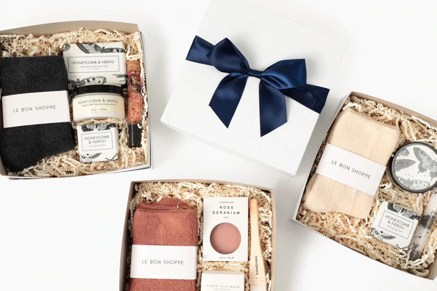 A white gift box tied with a navy ribbon beside two open boxes packed with socks, soaps and bath salts