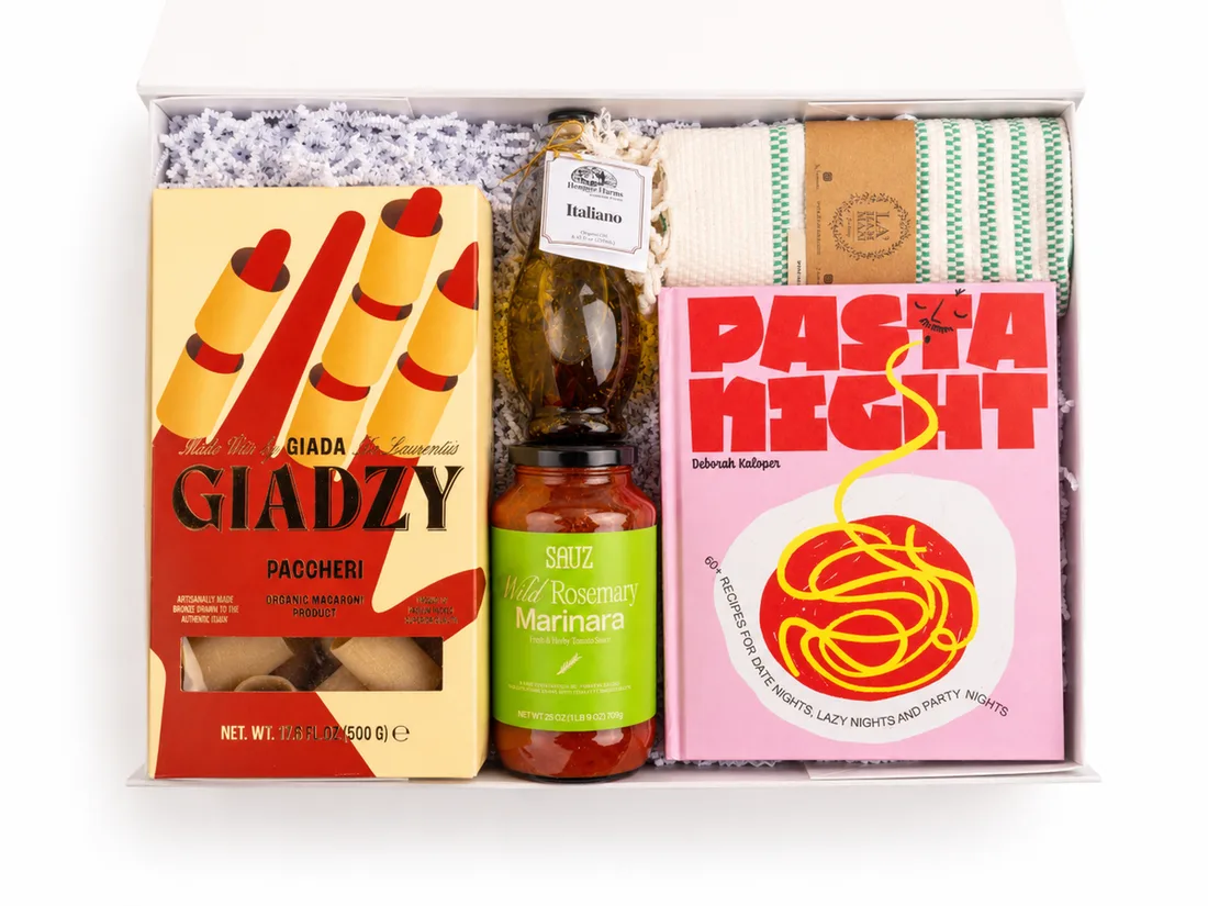White gift box holding artisan pasta, marinara, olive oil, a striped kitchen towel and a pasta cookbook